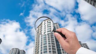 A hand holding a magnifying glass against the backdrop of an apartment.