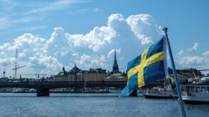 Sweden national flag waving, blur waterfront Stockholm buildings and blue sky background, sunny day,