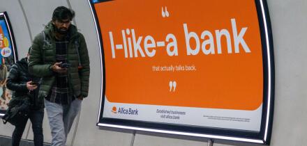 Commuters walk past an Advert for Allica Bank on wall of London railway station  London UK