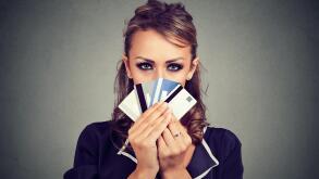 Serious woman hiding face behind many credit cards isolated on gray wall background