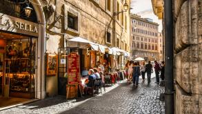 Tourists and local Italians enjoy afternoon shopping and dining at a sidewalk cafe patio on a narrow side street in the historic center of Rome Italy