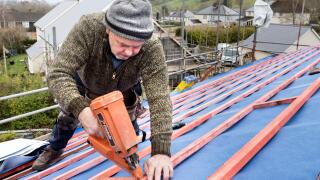 Roofer using a nail gun to fix batons on a new house roof, Llanfoist, Wales, UK