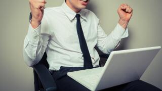 A young businessman is sitting in an office chair and is getting excited about his laptop