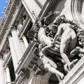 Close up of a group of marble statues on the facade of a french building, with a french flag waving in the background