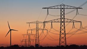 Silhouettes of a wind turbine and electric power posts during sunset