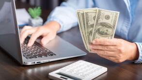 Close up young business woman using counting cash money one hundred dollar bills, checking financial documents, sitting at table with papers and tax f