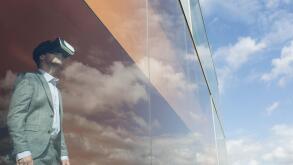 Businessman using virtual reality simulator glasses at modern window with cloud reflection