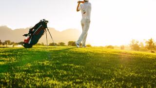 Low angle shot of professional golfer taking shot while standing on field. Full length of golf player swinging golf club on sunny day.