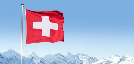 The flag of Switzerland fluttering in the wind with the Bernese Alps in the background, Grindelwald, Switzerland.