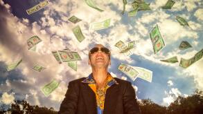 A man standing outside with money falling all around him