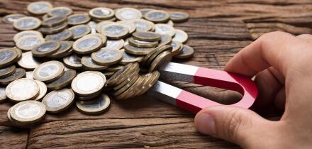 Cropped image of businessman's hand pulling coins with magnet on wooden table