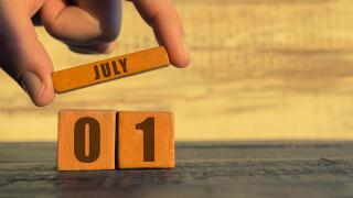 july 1st. Day 1 of month, calendar on a wooden cube. a woman's hand puts the name of the month on the number of the month on a wooden background summe