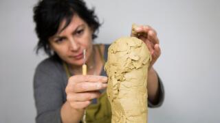Sculptor artist creating a bust sculpture with clay. She is happy of her work, she is concentrated, she is sculpting a woman.