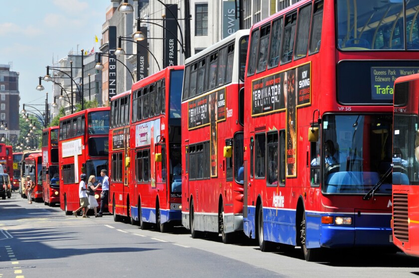 Pedestrians crossing Oxford Street between long queue of red London public transport double decker buses sunny summers day in West End England UK