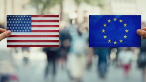 Two hands holding different flags, EU vs USA on politics arena over crowded street background. Future strategy, relations between countries. Cooperati