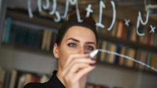 Educated business woman writing down mathmetical formula on glass