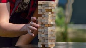 Guy sticks out wooden block from  tower of game jenga. Side front view. Concept. Surgut, Russia - September 25, 2019.