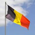 The national flag of Belgium flies up a flagpole on a beautiful summer day with a background of blue sky and white clouds.