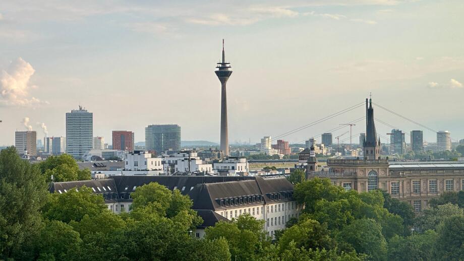 Dusseldorf skyline with Rheinturm tower, modern architecture, and the Rhine under a dramatic cloudy sky.