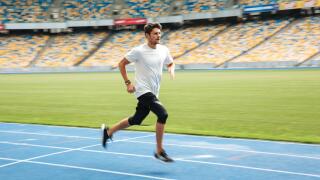 Side view of a young professional sprinter running on racetrack