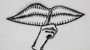 Graffito with closed mouth and a finger calling for silence