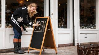 female small business owner making open sign outside wine shop