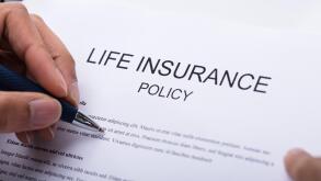Close-up Of A Person's Hand Filling Life Insurance Policy Form
