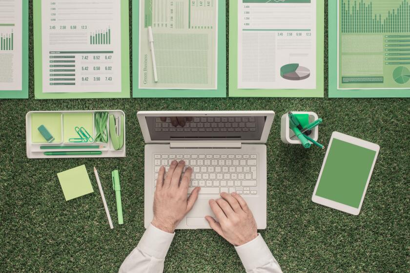 Businessman using a laptop and financial reports on lush grass: green business, sustainability and communication concept