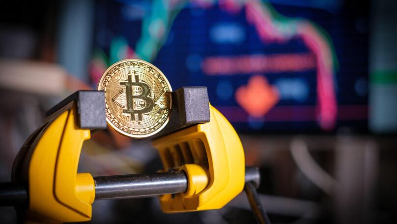 a bitcoin coin is clamped in a vice