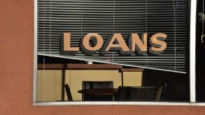 A quiet scene in a small town shows a loans sign in the window of a financial services storefront.