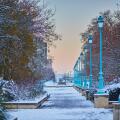 Winter cityscape of Paris with a snowy walkway lined with street lamps and trees, captured at sunrise