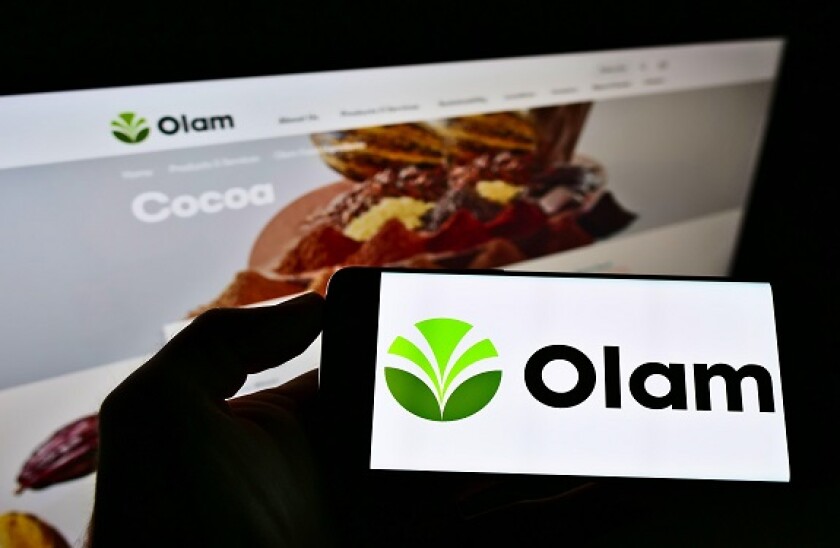 Person holding smartphone with logo of agribusiness company Olam International Limited on screen in front of website. Focus on phone display.