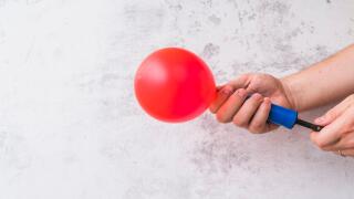 Close up hand blowing red balloon with pump against wall