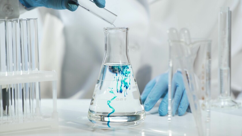 Chemist pouring substance into conical flask with liquid, chemical experiment