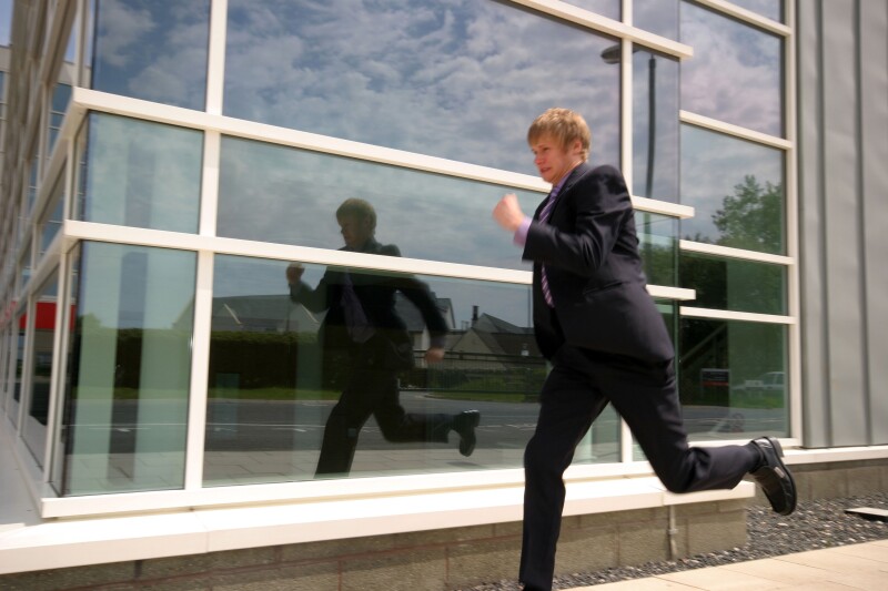 A Stock Photograph of a Young Adult Businessman Outside a Modern Office Block Running