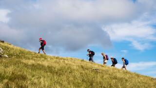 Line of hikers hiking up a hill following a leader on Moel Lefn"s grassy mountainside in Snowdonia National Park. Gwynedd, Wales, UK, Britain