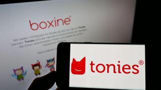 Person holding smartphone with logo of German audio toys company Boxine GmbH (Tonies) on screen in front of website. Focus on phone display.