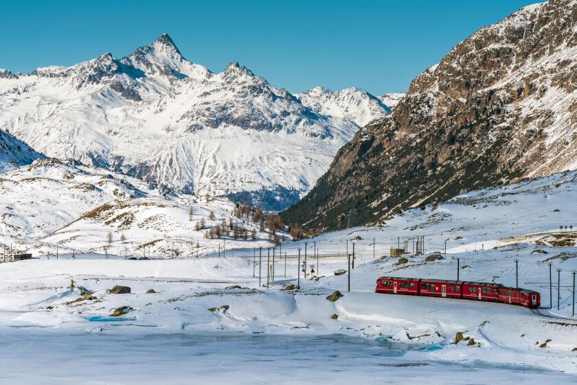 Bernina Express red train passing Lago Bianco in a scenic winter mountain landscape, Graubunden, Switzerland