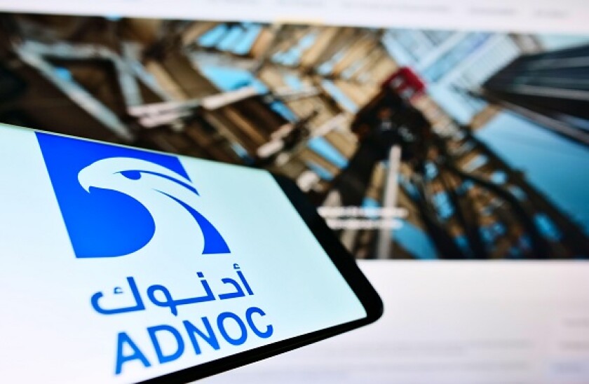 Mobile phone with business logo of Abu Dhabi National Oil Company (ADNOC) on screen in front of website. Focus on center-right of phone display.