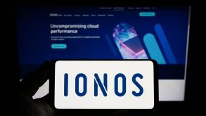 Person holding smartphone with logo of German web hosting company Ionos SE on screen in front of website. Focus on phone display.