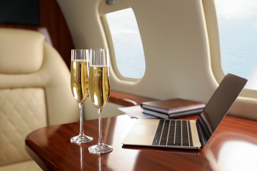 Glasses of champagne with laptop and notebooks on table in airplane-adobe