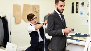 Portrait of handsome young man being fitted in bespoke suit by tailor in traditional atelier studio