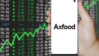 A man holds a smartphone displaying the logo of company Axfood listed on OMX Stockholm. Positive stock market background. Credit: PIXDUCE