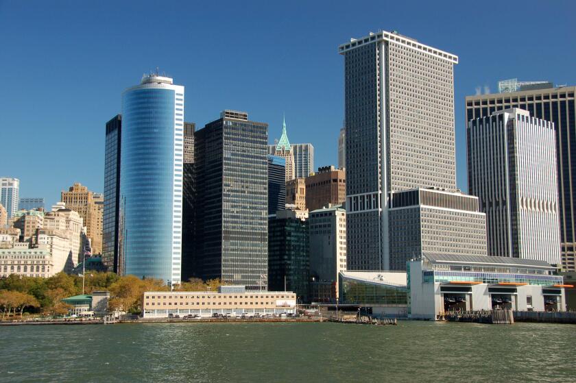 Modern skyscrapers line the waterfront in Lower Manhattan?s Financial District, New York City, with clear blue skies and calm water below