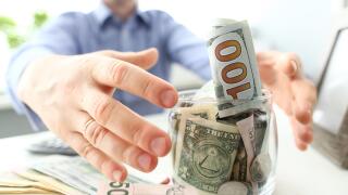 Male hands grabbing big fat jar full of US currency as greed gesture