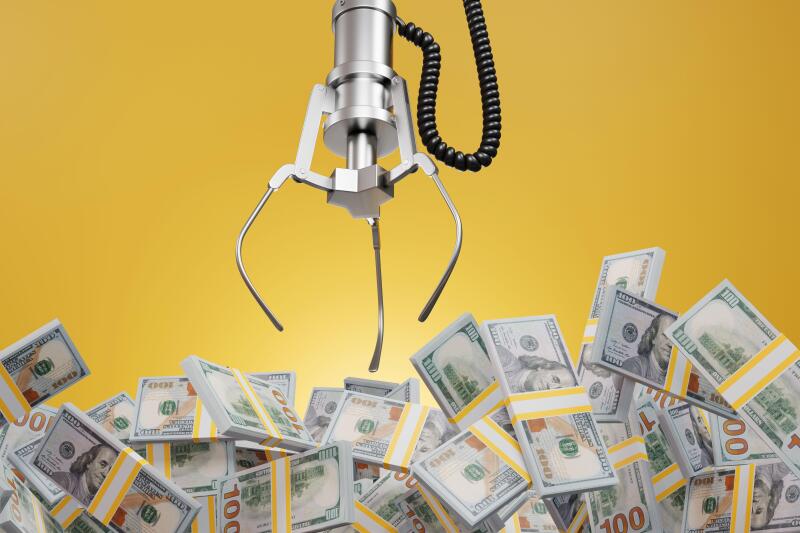 Robotic claw of grab machine is grasping stacks of one hundred US dollar bills. Earning profit, successful investment and business competition