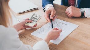 cropped shot of businessman pointing at signature place in loan agreement near woman holding dollar banknotes