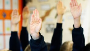 School children with hands up in the air wanting to answer a question