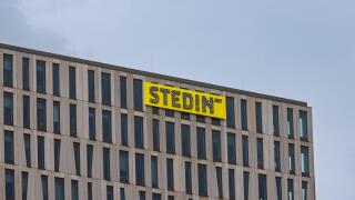 The top corner of the modern Stedin office building, showing its distinctive facade and the company's bright yellow logo against a grey sky. Rotterdam