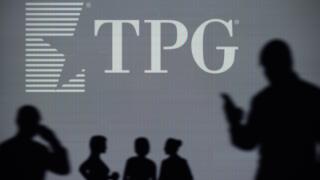 The TPG Capital logo is seen on an LED screen in the background while a silhouetted person uses a smartphone (Editorial use only)